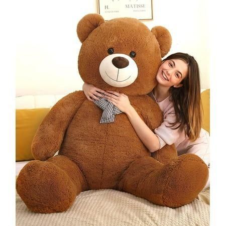 Woman hugging a large brown teddy bear on a bed with a blurred background