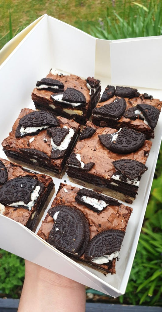 Box of Oreo brownies held by a person with greenery in the background
