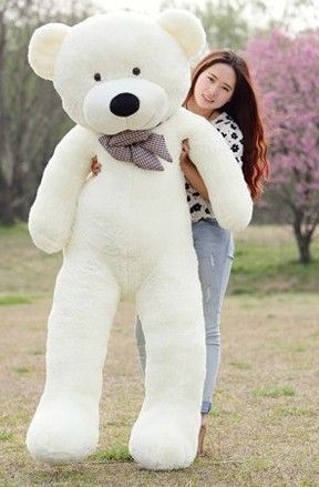 Person holding a large white teddy bear in an outdoor setting with trees and grass.